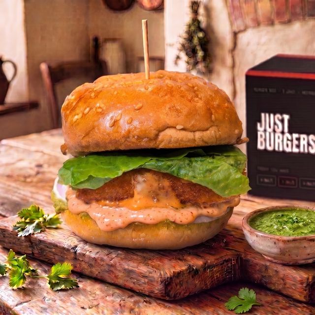 The No.2 Paneer burger on a wooden board — a crumb-fried paneer slab with lettuce and orange spiced mayo in a sesame bun, green chutney beside it.